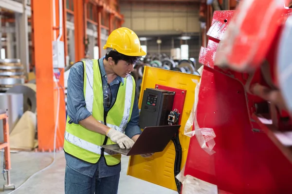 asian man engineer technical department using laptop working in power plant control panel of industry factory. male professional system electrician machine control with computer laptop.