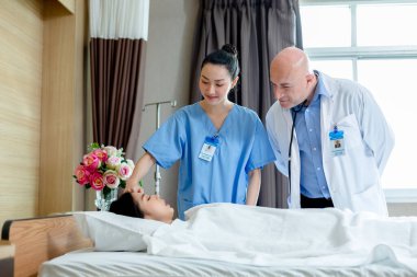 Doktor ve hemşire hastane yatağında semptomlu kadın hastayı inceliyor. Doktor, hastanede tedaviyi kontrol et..