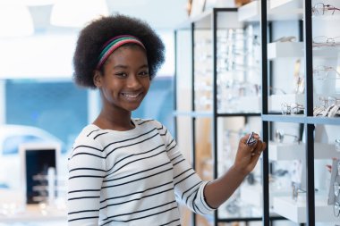 happy young woman African american afro hair smile holding spectacles standing at optical shop. modern ophthalmologist concept.