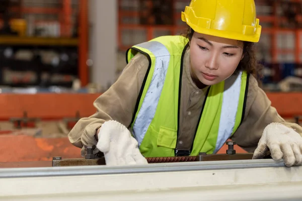 Asian female workers wear red helmet working check up iron production in factory. woman in heavy Industrial manufacturing workplace.
