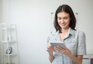 Güzel bir kadın gülümsüyor ve tablet üzerinde çalışırken ona bakıyor. İş kadını dijital tablet çevrimiçi işi veya bilgi taraması kullanıyor.