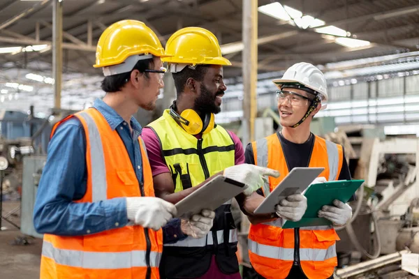 3人の工業技術者は重工業製造業内の工場のタブレット トーキング プロジェクトを使用してハード ハットと制服を着用する 従業員への指導業務 ロイヤリティフリーのストック画像