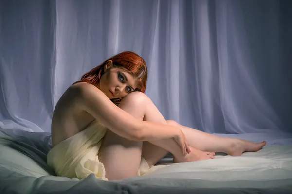 Młoda kobieta siedzi na łóżku w arkuszach — Zdjęcie stockowe