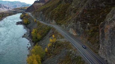 Mavi araba nehir boyunca dağlarda yol boyunca gider. Coupe. Havadan üst görünüm