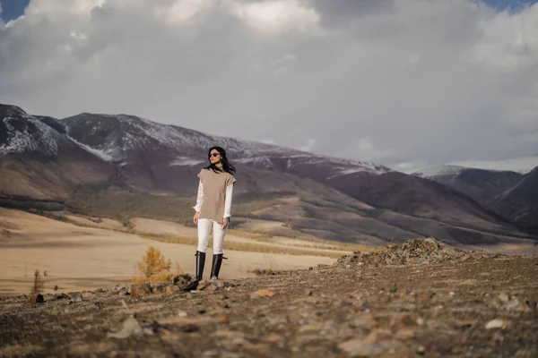 Krásná stylová dívka pózující na pozadí bílých zasněžených vrcholků. Slunečný Royalty Free Stock Obrázky