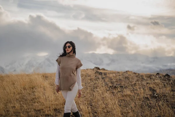 Menina elegante bonita posando contra o pano de fundo de picos nevados brancos. Ensolarado Fotografia De Stock