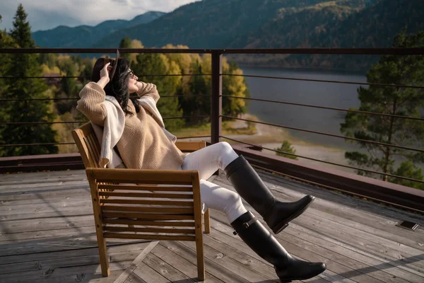 Menina bonita em roupas leves elegantes e chapéu marrom senta-se no telhado em raios de sol e frio Fotografia De Stock