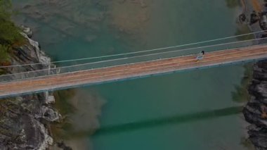 Güzel bir turist kız nehrin karşısındaki yaya köprüsünde yürüyor. Uçan İHA 'nın en üst görüntüsü