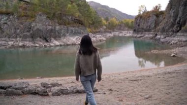 Siyah saçlı güzel kız nehir boyunca bir turist yürüyor. Sonbahar sarı ağaçları kayalar