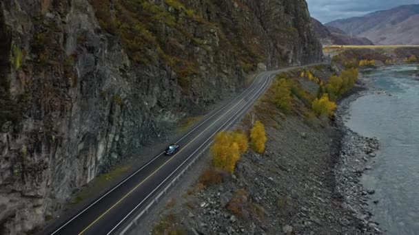 Блакитний автомобіль їде по дорозі в гори вздовж річки. Купе. Вид зверху повітря — стокове відео