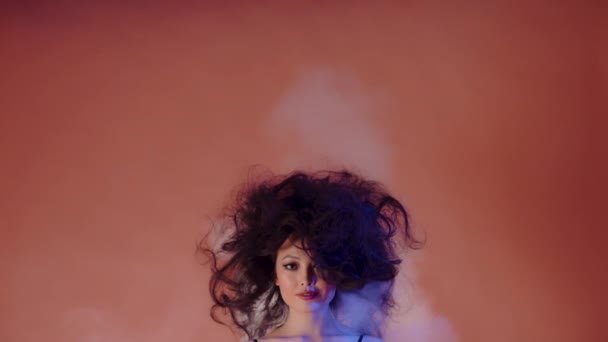 Mädchen asiatischen Aussehens steht auf farbigem Hintergrund mit zerzausten Haaren. Rauch steigt aus den Haaren — Stockvideo