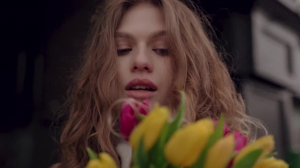 Nettes Mädchen im weißen Mantel mit einem Strauß Tulpen blickt in die Kamera. Frühling und Tulpen. Nahaufnahme — Stockvideo