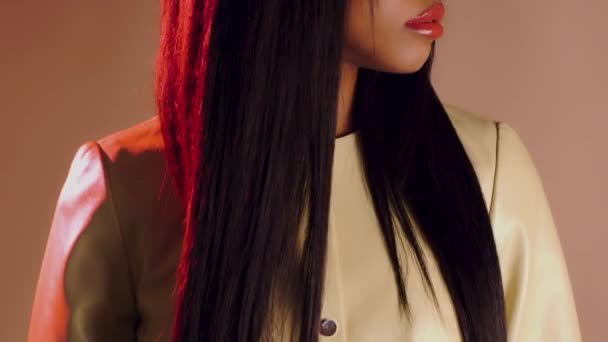 Красивая девушка с красными губами и длинными черными волосами в желтом кожаном пальто поворачивает голову — стоковое видео
