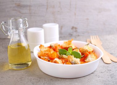 Balkabağı parçalanmış ve ekmek, kuru otlar, zeytin yağı ve balkabağı tohumlarıyla pişirilmiş gri arka planda beyaz bir tabakta..