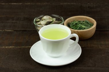 Beyaz fincanda limon çayı ve ahşap arka planda yeşil yaprakla dilimlenmiş limon çimi. Sağlıklı bitkisel içecek kavramı.