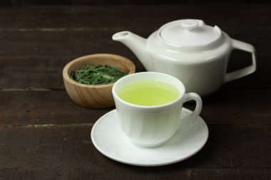 Beyaz fincanda limon çayı ve ahşap fonda beyaz çaydanlık olan ahşap kasede limon yaprağı. Sağlıklı bitkisel içecek kavramı.