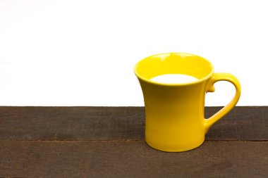 Tahta ve beyaz arka planda sarı süt bardağı.