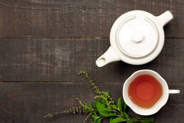 Tulsi ya da beyaz bardakta kutsal fesleğen çayı ve ahşap arka planda taze tütsü dalı olan çaydanlık. Hindistan 'da Ayurvedic tıp.