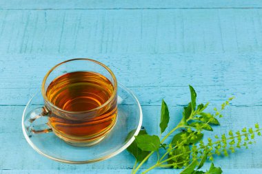 Tulsi ya da şeffaf cam fincanda mavi ahşap kaplamalı taze tütsü yaprağı olan kutsal fesleğen çayı. Hindistan 'da Ayurvedic tıp.
