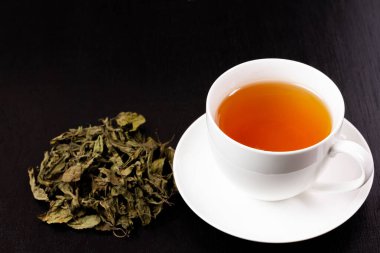 Tulsi ya da beyaz fincanda siyah ahşap zemin üzerinde kurumuş tül yaprağı yığını olan kutsal fesleğen çayı. Hindistan 'da Ayurvedic tıp.