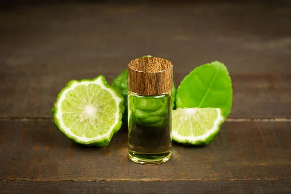 Şişede Bergamot yağı ve ahşap arka planda yeşil yapraklı taze bergamot meyvesi..