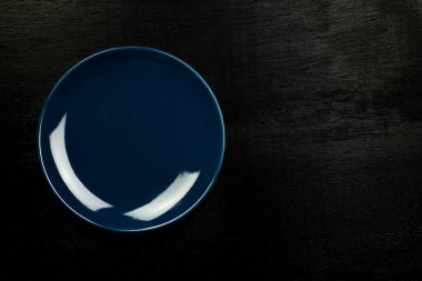 Ahşap zemin üzerinde mavi boş tabak, üst görünüm, fotokopi alanı ile koyu ton. Seramik kaplama. 