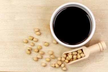 Soya sosu küçük beyaz kâse içinde soya fasulyesi ve tahta kaşıkla kahverengi ahşap arka plan, üst manzara. Soya sosu pişirme malzemesidir..