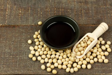 Soya sosu küçük siyah kasede soya fasulyesi ve tahta kaşıkla kahverengi ahşap arka plan, üst manzara. Soya sosu pişirme malzemesidir..
