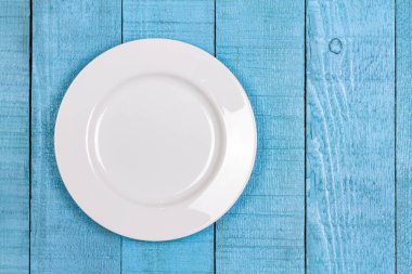 Mavi ahşap zemin üzerinde boş beyaz seramik plaka, üst görünüm, boşluk kopyala.