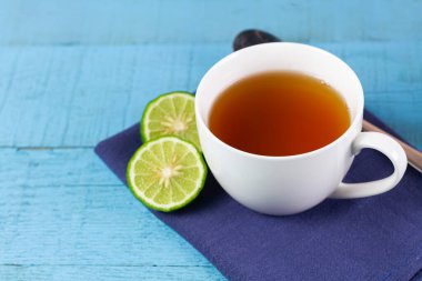 Bergamot çayı veya beyaz fincanda Earl Grey çayı ve mavi ahşap masada dilimlenmiş taze bergamot meyvesi..