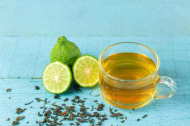 Bergamot çayı ya da şeffaf fincanda Earl Grey çayı ve mavi ahşap masada dilimlenmiş taze bergamot meyvesi..