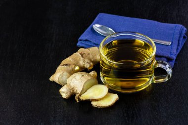 Cam bardakta zencefil çayı ve siyah ahşap arka planda izole edilmiş taze zencefil. Bilimsel adı zingiber officinale. Sağlık hizmetleri konsepti için bitkiler.