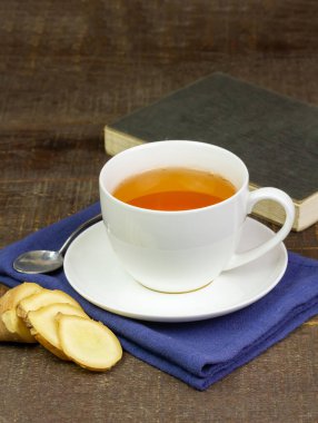 Beyaz seramik bardakta zencefil çayı ve ahşap zemin üzerinde dilimlenmiş taze zencefil. Bilimsel adı zingiber officinale. Sağlık hizmetleri konsepti için bitkiler.