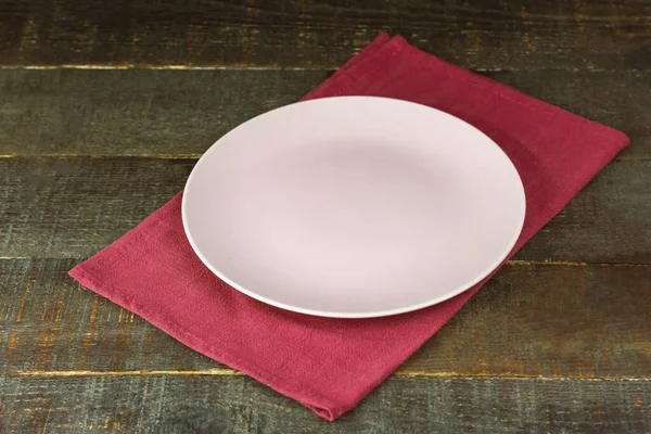 Kırsal ahşap masada kırmızı masa örtüsü üzerine boş pembe tabak..
