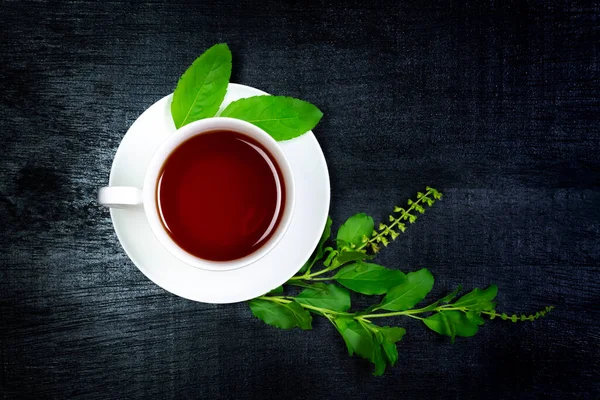 Tulsi ya da beyaz fındıklı kutsal fesleğen çayı. Taze tütsü dalı ve siyah ahşap arka planda yaprak. Üst manzara, koyu renk. Hindistan 'da Ayurvedic tıp.