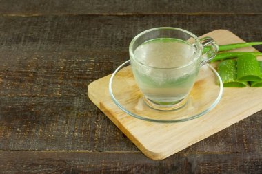 Şeffaf bardakta Aloe Vera suyu ve rustik ahşap masada taze aloe vera. Sağlık için iç..