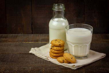 Kırsal ahşap arka planda çikolatalı kurabiyeli yakın bardak süt..