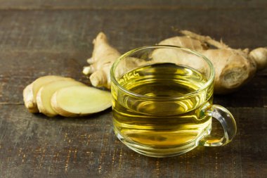 Şeffaf bardakta zencefil çayı ve ahşap zemin üzerinde dilimlenmiş taze zencefil. Bilimsel adı zingiber officinale. Sağlık hizmetleri konsepti için bitkiler.