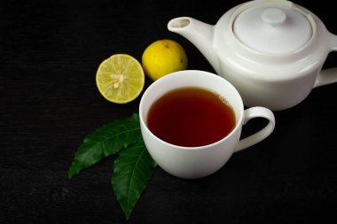 Neem yaprağı ve limonlu seramik fincanda siyah ahşap arka planda koyu tonda çay..