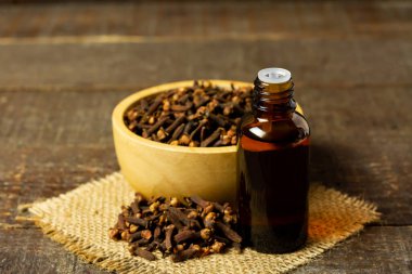 Şişe içindeki karanfil yağı ve ahşap arka plandaki ahşap kasede kuru karanfil..