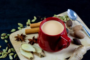 Kırmızı fincanlı Masala çayı zencefil, kakule, tarçın, hindistan cevizi ve anason ile siyah ahşap arka planda. Masala chai popüler geleneksel Hindistan içeceği süt, çay ve baharattan yapılmıştır..