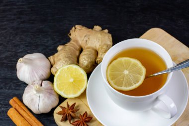 Siyah ahşap zemin üzerinde öksürük ilacı olarak sarımsak, zencefil ve limonlu sıcak çay..