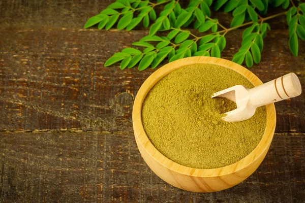 Ahşap kasede moringa tozu kepçeyle ve ahşap arka planda taze yeşil yaprak.
