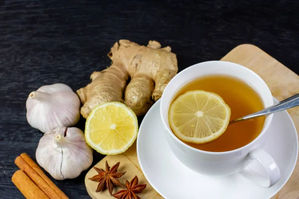 Siyah ahşap zemin üzerinde öksürük ilacı olarak sarımsak, zencefil ve limonlu sıcak çay..