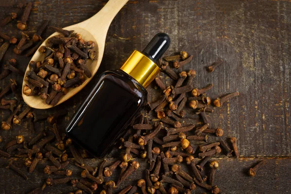 Şişe içindeki karanfil yağı ve ahşap kaşık üzerindeki kuru karanfil kırsal ahşap arka plan, üst manzara..