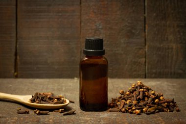 Şişe içindeki karanfil yağı ve ahşap arka planda tahta kaşıkta kuru karanfil..