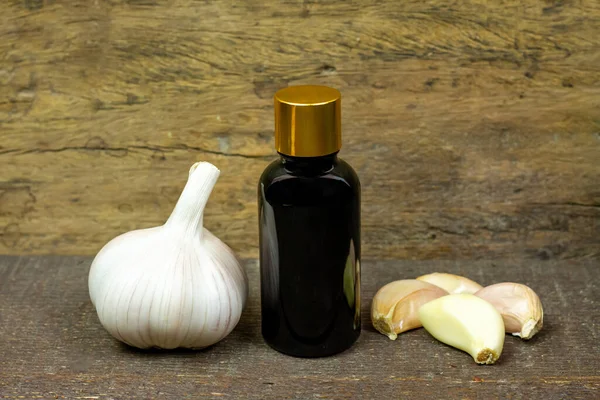 stock image Garlic Oil in bottle and fresh garlic on wooden background. 