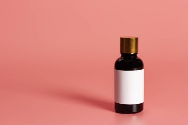 Pembe arkaplan üzerinde boş etiket maketi olan şişe.