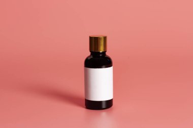 Pembe arkaplan üzerinde boş etiket maketi olan şişe.