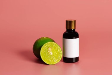 İçinde boş etiket maketi ve pembe arka planda taze limon olan bir şişe. Temel petrol konsepti.